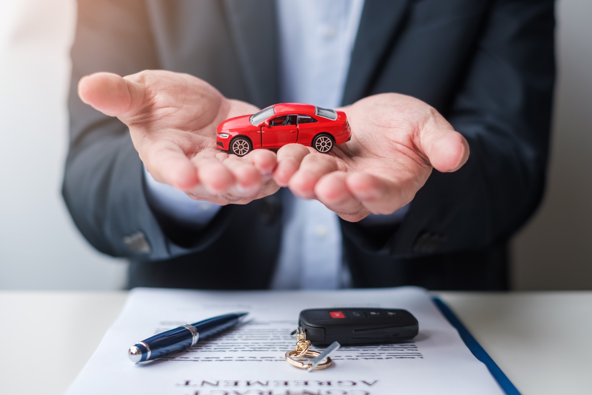 Businessman hand holding red car toy with vehicle keyless, pen and contract document. buy and sale, insurance, rental and contract agreement concepts